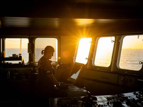 La coordinatrice de la recherche et du sauvetage à bord du bateau observe un radar sur la passerelle alors que le jour commence à se lever à l'extérieur.