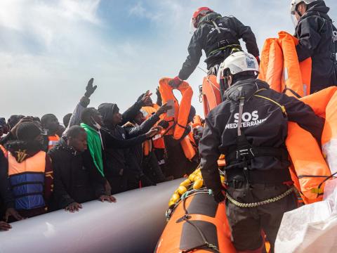 Des membres de l'équipe de recherche et de sauvetage distribuent des gilets de sauvetages aux occupants d'un bateau pneumatique surchargé sur lequel se trouvent une centaine de migrants, hommes, femmes et enfants, fuyant la Libye.