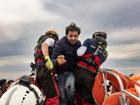 Un rescapé quitte l'embarcation surchargé sur laquelle il vient d'être secouru. Il est aidé par des membres de l'équipe de recherche et de sauvetage à monter à bord du semi-rigide d'intervention.