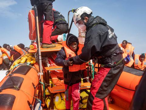 Un membre de l'équipe de recherche et de sauvetage aide un jeune garçon a se déplacer sur le semi-rigide de sauvetage. Il vient d'être évacué d'une embarcation pneumatique surchargée en détresse.