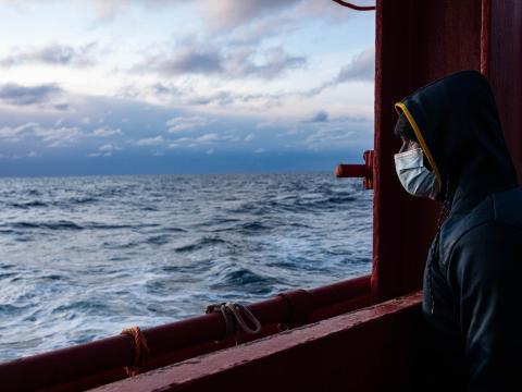Un rescapé secouru d'un bateau en détresse portant une veste à capuche regarde l'horizon et la mer depuis le pont du bateau.