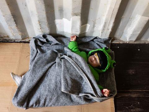 Un bébé enroulé dans une couverture et posé sur un carton dort dans un des containers du bateau pour l'abriter du vent.