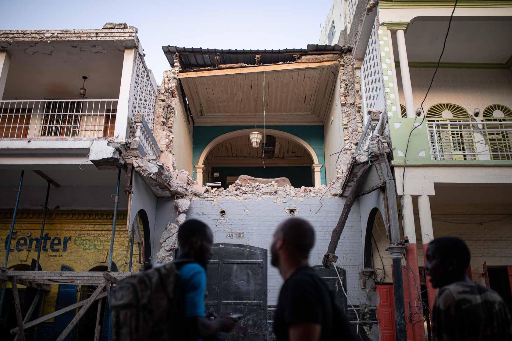 Trois hommes observent la façade détruite d’un immeuble d’habitation dans le centre historique. Jeremie, Haïti. Septembre 2021
