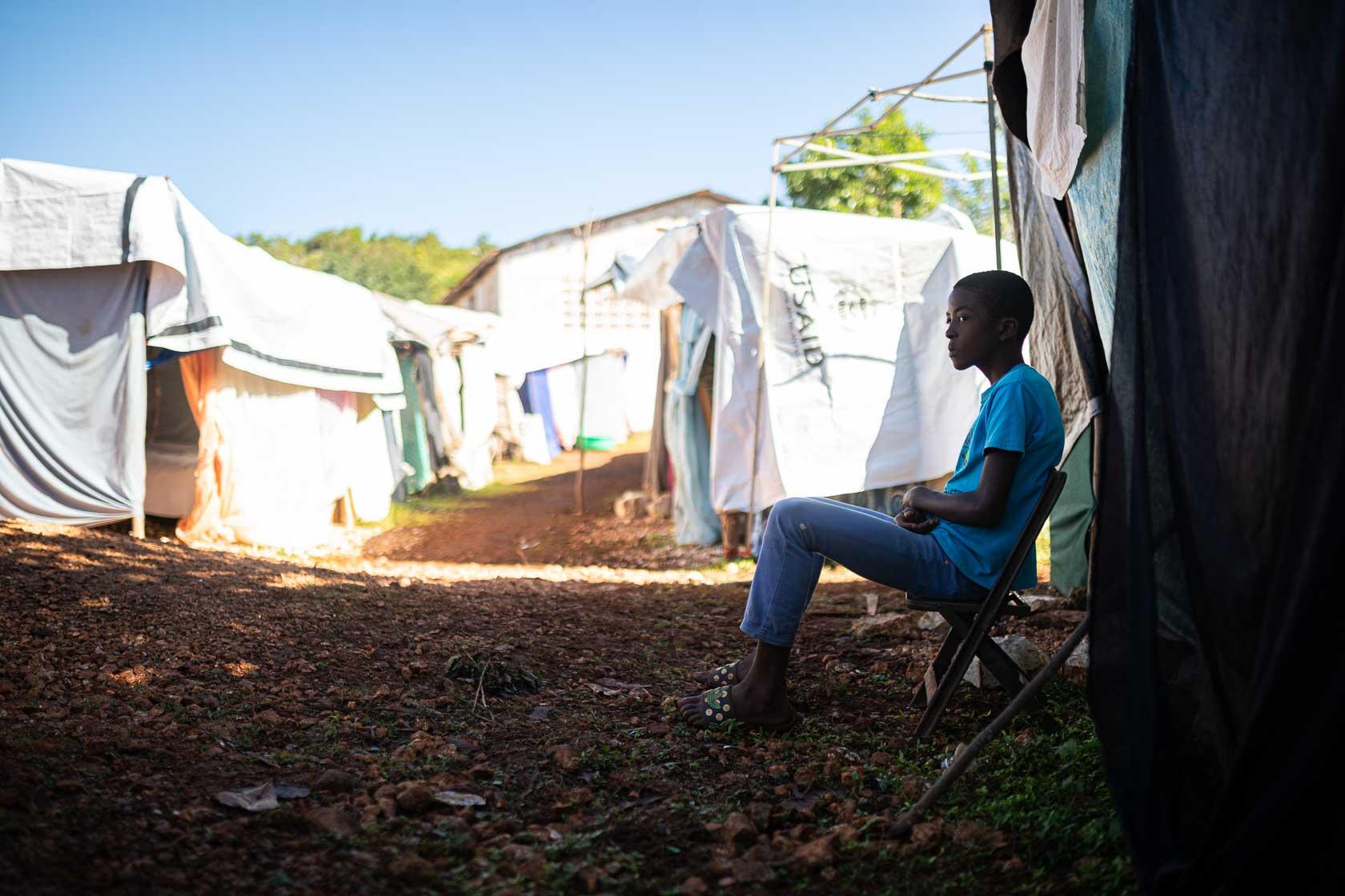 Un adolescent est assis devant la tente qui lui sert de logement à la suite du séisme. Région de Pestel, Haïti. Septembre 2021