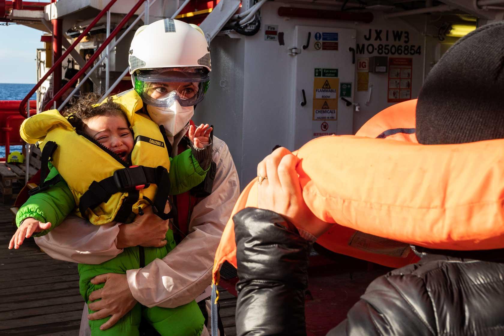 Blandine, sage-femme de l’équipage, prend en charge un bébé qui vient d’être secouru pendant que la mère de celui-ci ôte son gilet de sauvetage. Méditerranée Centrale. Mars 2021