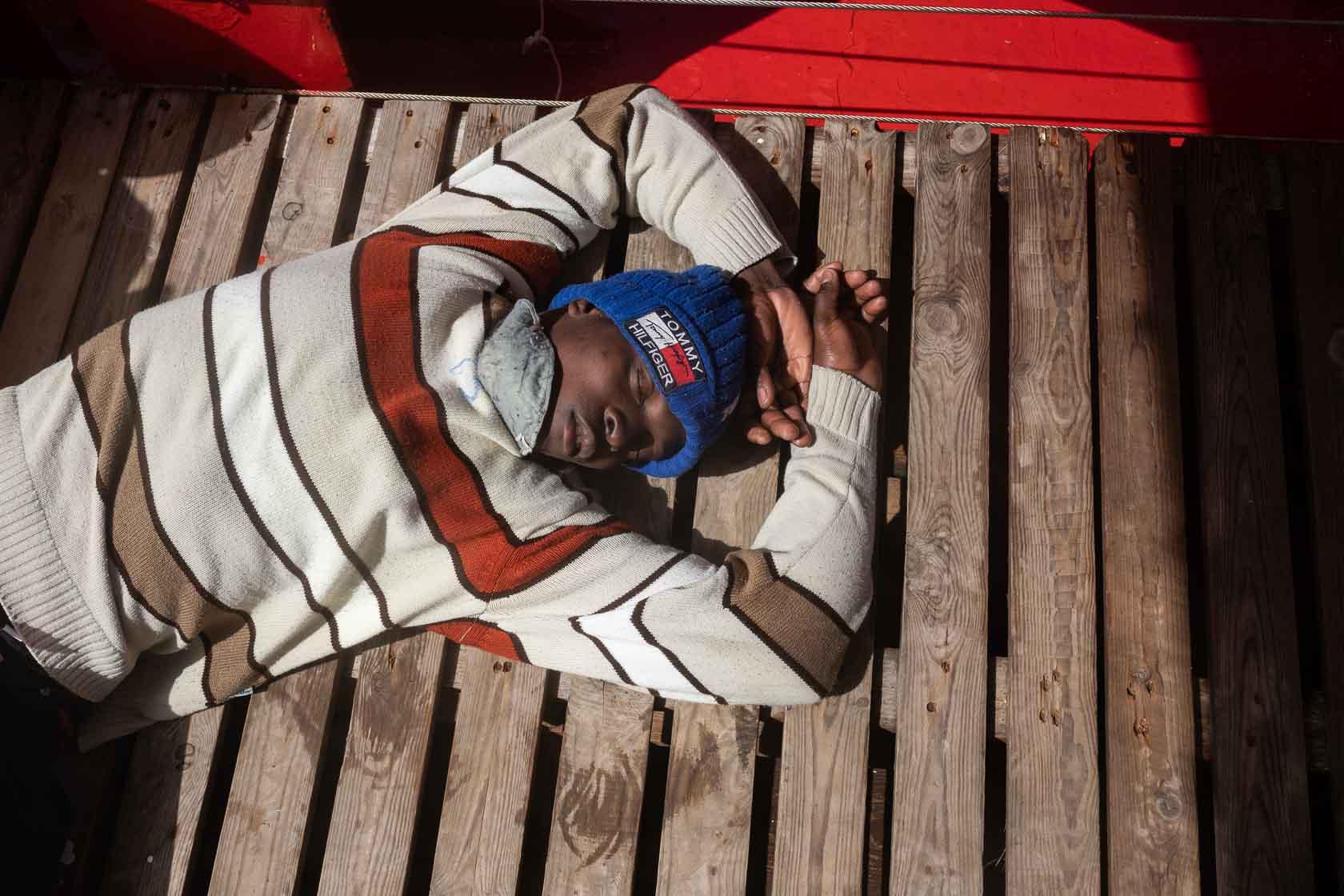 Un jeune rescapé épuisé dort sur le pont du bateau après avoir été secouru. Augusta, Italie. Mars 2021