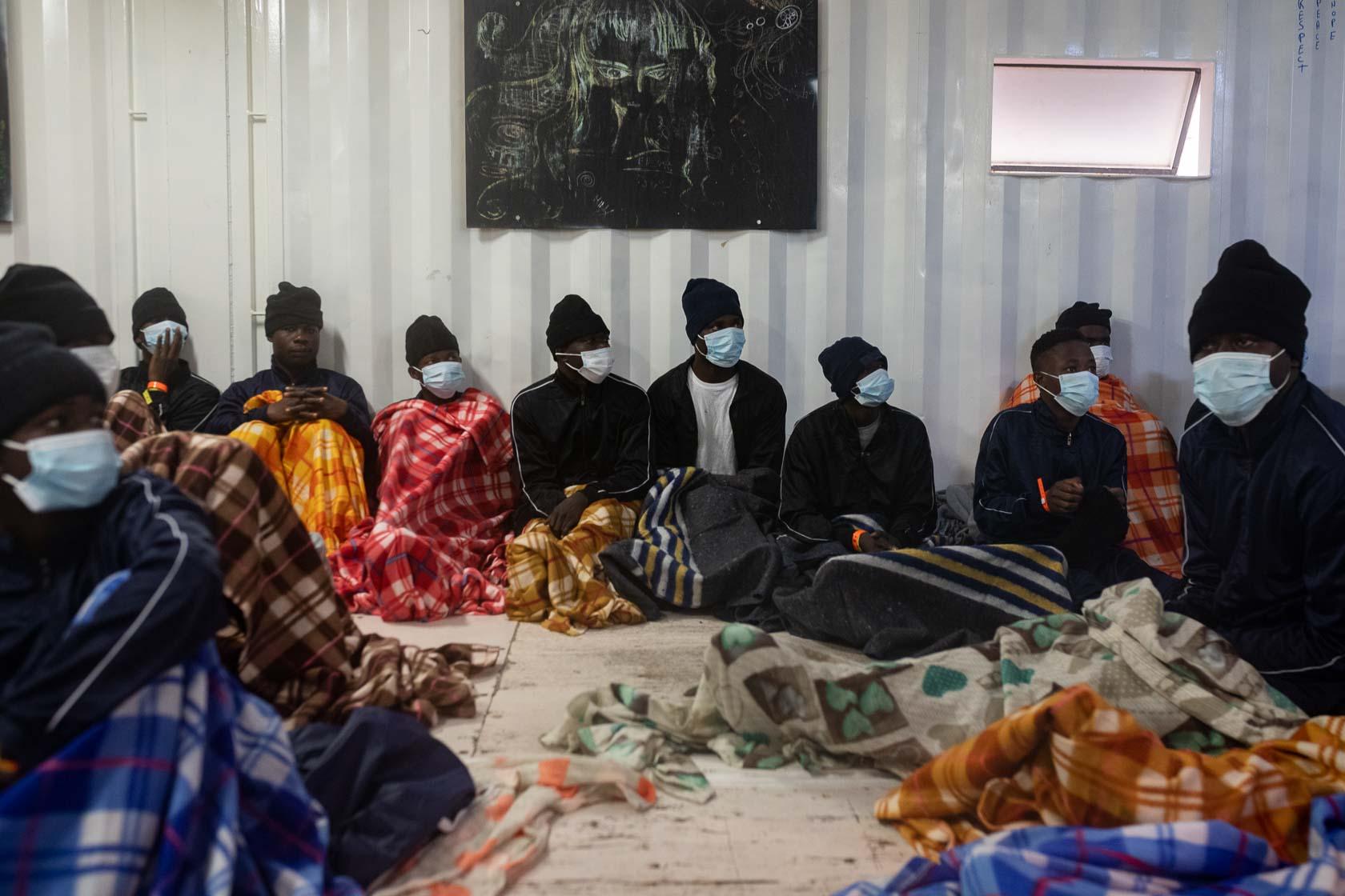 Des rescapés écoutent des consignes liées à la vie à bord dans le « men’s shelter » où dorment tous les hommes secourus. Méditerranée Centrale. Mars 2021