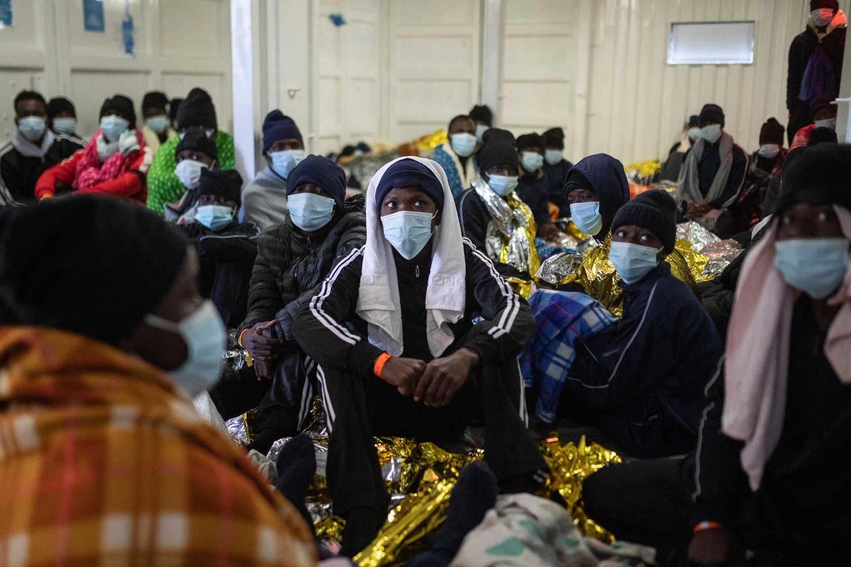Des rescapés écoutent des consignes liées à la vie à bord dans le « men’s shelter » où dorment tous les hommes secourus. Méditerranée Centrale. Mars 2021