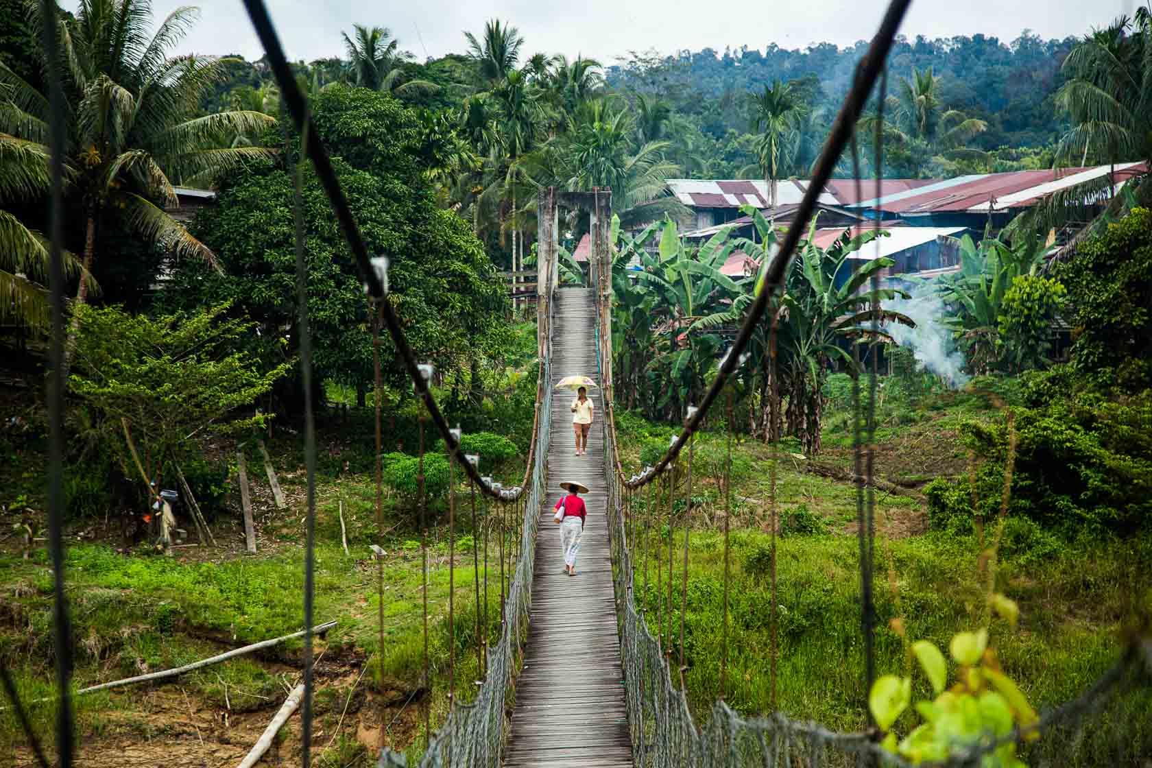 Deux femmes marchent sur un pont suspendu à l'entrée du village de Punan Bah, zone très touchée par l'accaparement des terres des communautés autochtones Punan Bah, Sarawak, Malaisie - 2015